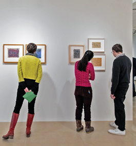 A man and two women, photographed from behind, look closely at artwork on a wall in the Rose Art Museum